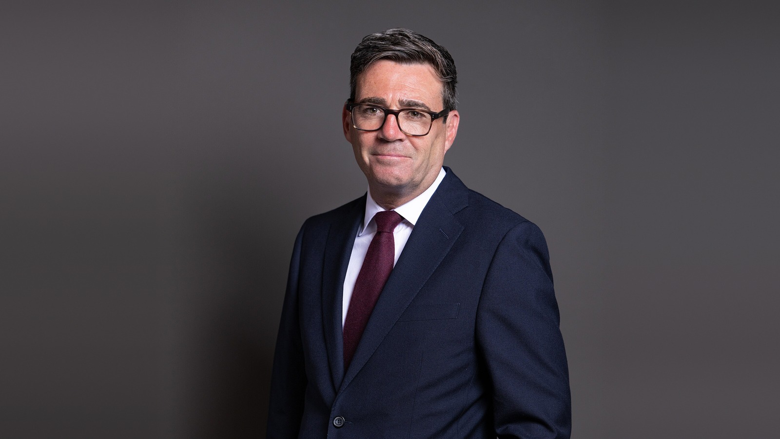 Porträtt av Storbritanniens premiärminister Andy Burnham i mörk kostym och vinröd slips.